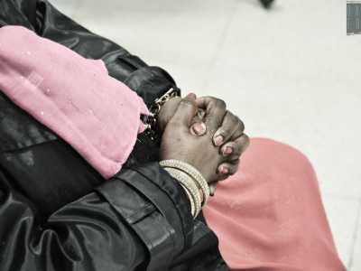 Un particolare della donna: le mani incrociate poggiate sulla lunga gonna rosa